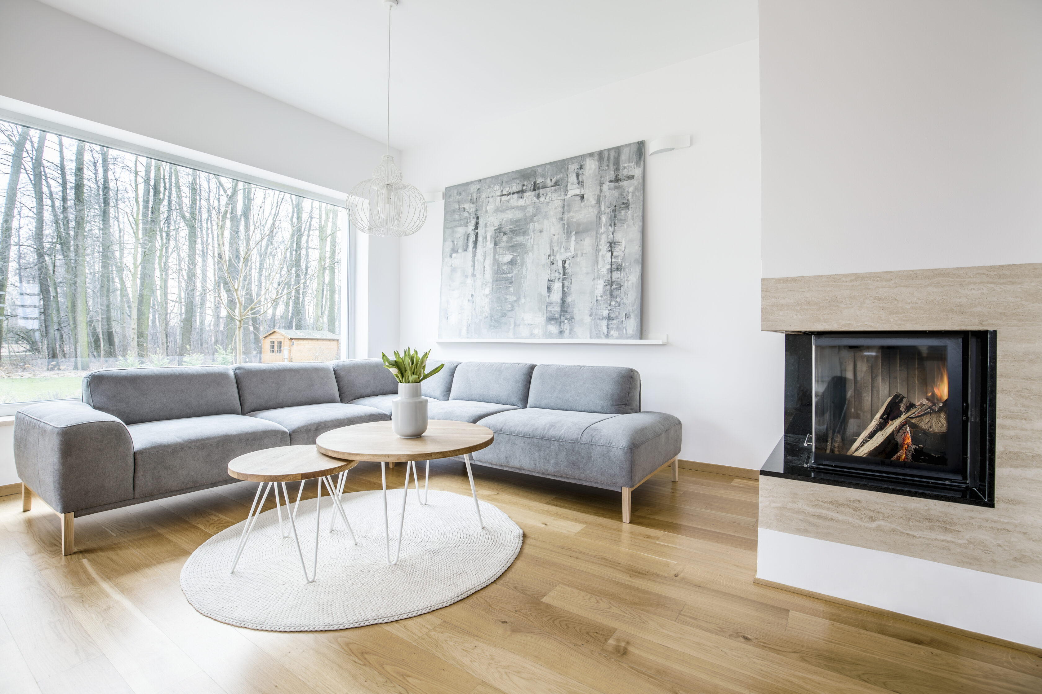 Wooden table on a round rug near sofa in spacious living room interior with fireplace and painting