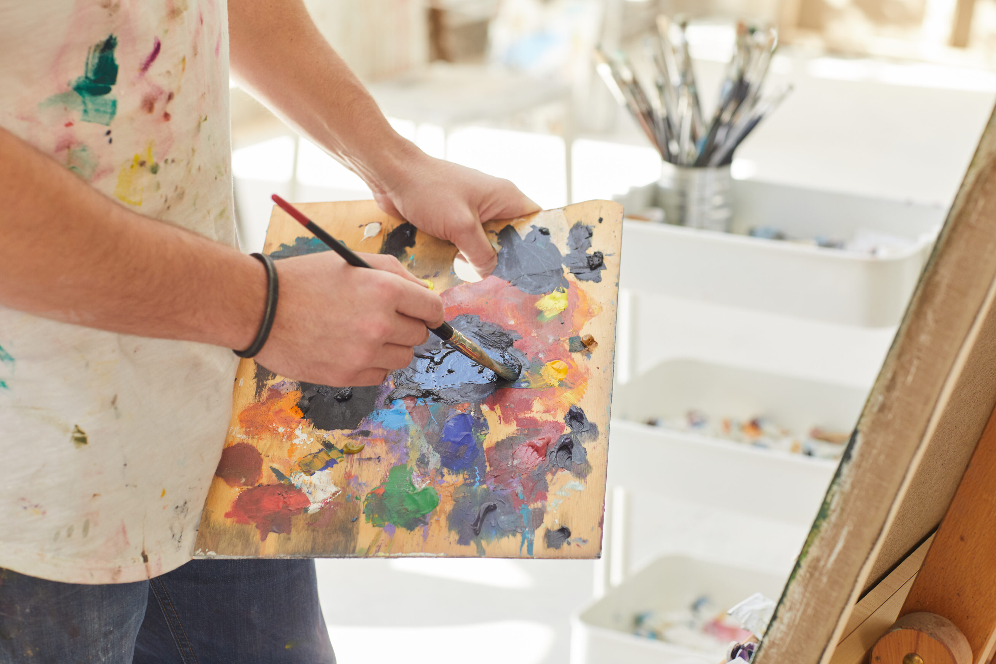 Close up of unrecognizable male artist holding palette and mixing paint while painting picture in art studio, copy space